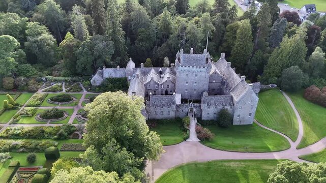 Elevated frontal aerial drone video of 15th-century Cawdor Castle featuring formal flower gardens, stone tower house, manicured lawns, and surrounding forest in Nairnshire, Scottish Highlands,Scotland