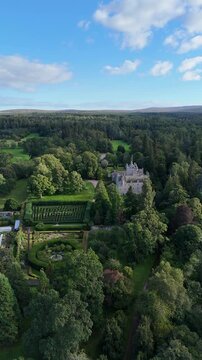 High vertical aerial drone video of 15th-century medieval Cawdor Castle featuring its famous hedge maze, manicured gardens, and vast surrounding forest in Nairnshire, Scottish Highlands, Scotland