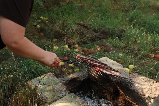Person holding a wire grill basket over hot coals in an improvised stone fire pit