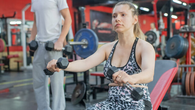 A Caucasian woman with cerebral palsy exercises with dumbbells in a gym.