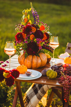 Beautiful elegant autumn table setting for thanksgiving family dinner or wedding. Orange pumpkin with flowers as centrepiece. Cozy fall home atmosphere. Wineglass, romantic marriage proposal, sunset