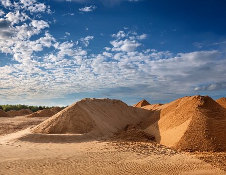 open construction site with sand dune and earth piles under sky with blue and white cloud formations