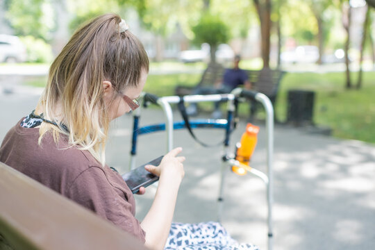 A Caucasian woman with cerebral palsy sits on a park bench.