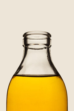 Open glass bottle neck with golden yellow liquid on neutral background, minimalist close up studio image with copy space for text, organic oil, vinegar or juice product packaging mock up concept.