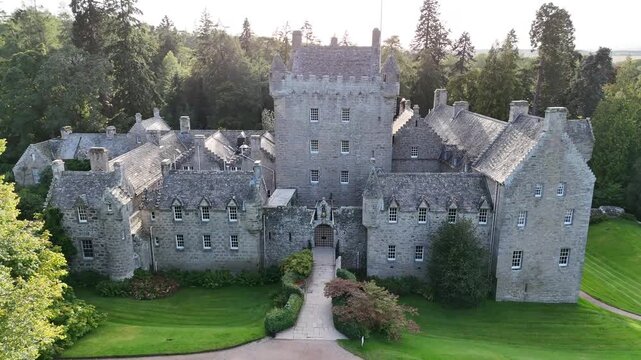 Elevated wide aerial drone video of 15th-century medieval Cawdor Castle featuring its stone tower house, main entrance, manicured lawns, and surrounding forest in Nairnshire, Scottish Highlands, Scotl