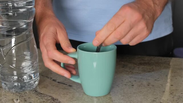 Male hands mixing a warm beverage with a teaspoon inside a ceramic cup on a kitchen counter