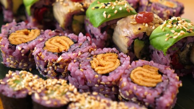 Colorful sushi rolls cover gourmet platter, with sesame crusted pieces, avocado slices, and purple rice maki packed together. Sushi platter shows rich, celebratory presentation built for sharing.