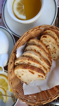 Toasted bread slices rest in wicker basket as fingers remove one piece from front. White cups of tea with lemon and simple dishes frame quiet morning meal setting with crust and grain texture.