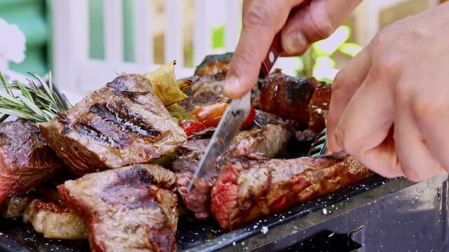 Close up of chef cutting steak on variety meat platter at outdoor Argentine parilla