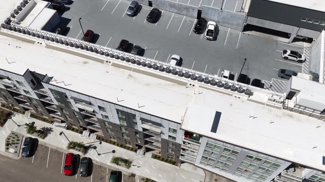 Top down aerial of urban roof top parking lot and multistory buildings in day with multiple cars parked
