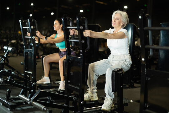 Positive sporty elderly woman using standing abductor machine to stay fit, strengthen hips, and maintain mobility, independence, and healthy aging