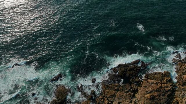 Mesmerizing top-down aerial view of turquoise Atlantic waves crashing against rugged, sun-drenched coastal rocks near A Guarda, evoking a powerful sense of raw natural energy, coastal serenity, and