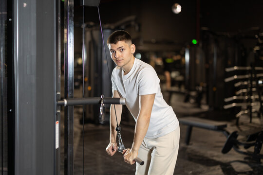 Motivated young man intensely training triceps, pushing cable bar with control and focus during strength session at modern gym..