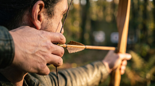 Archer aims bow and arrow outdoors in forest setting with blurred background