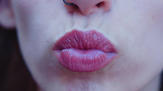 A beautiful young woman's full, pink-painted lips blowing a kiss in a close-up, slow-motion shot