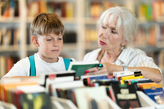 Happy senior woman and boy choosing books from display case table in bookstore
