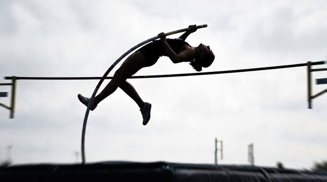 Athlete Silhouetted During Pole Vault Jump Against Cloudy Sky
