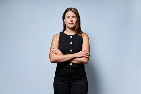 Confident businesswoman standing with arms crossed on light blue background
