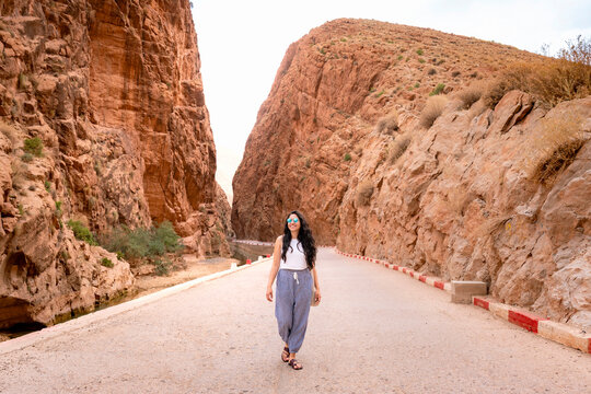 Young Latin woman walking on a winding road through the scenic Dades Gorge canyon exploring the unique landscapes and red rock formations of the Atlas Mountains