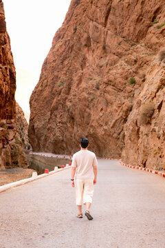 Man walking on a road through the dramatic red rock walls of Todra Gorge exploring the rugged natural beauty and adventure of the Atlas Mountains in Morocco