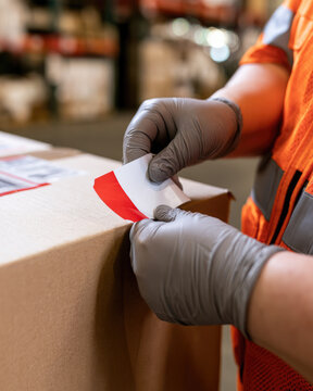 Shipping clerk applying red tilt sensor label to corrugated carton with gloved hands