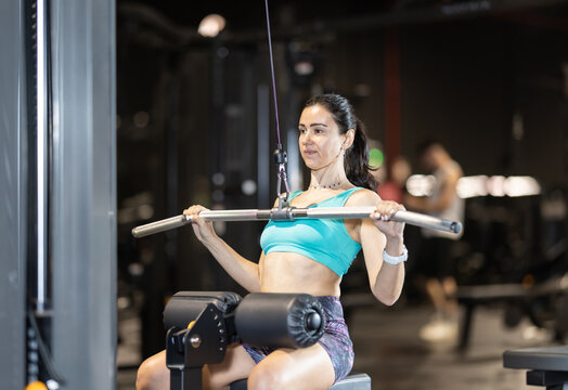 Focused woman performing wide-grip lat pulldown on cable machine to strengthen upper back and improve posture during workout at gym