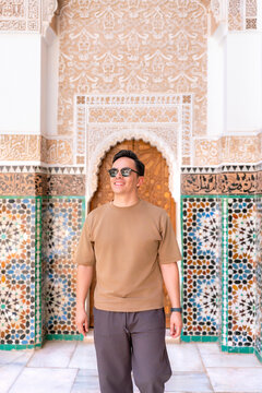 Young Latino man enjoying architecture and mosaic patterns during a solo travel trip to Ben Youssef Madrasa in Marrakech Morocco exploring cultural heritage