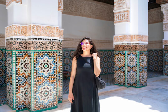 Young Latina woman smiling and looking up while exploring the ornate Islamic architecture and colorful mosaic tiles of Ben Youssef Madrasa in Marrakech enjoying cultural travel