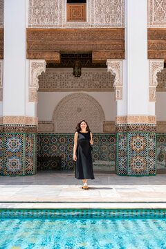 Young woman smiling standing in a historic Ben Youssef Madrasa courtyard in Marrakech Morocco featuring intricate Islamic architecture colorful zellige tiles and a reflecting pool