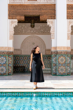 Young woman smiling and walking by the pool in the historic Ben Youssef Madrasa admiring the traditional Moroccan architecture and detailed mosaic patterns