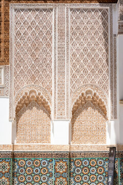Ben Youssef Madrasa wall displaying intricate stucco carvings and arabesque patterns above colorful geometric zellij mosaic tiles highlighting Moroccan Islamic architecture and craftsmanship