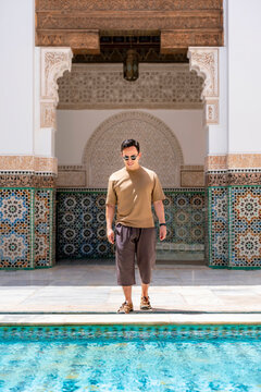 Young man standing by the serene reflecting pool in the historic Ben Youssef Madrasa courtyard enjoying Moroccan architecture and traditional tilework during his travels