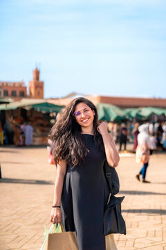 Young woman smiling and carrying shopping bags while exploring the vibrant market square of Jemaa el Fnaa in Marrakech experiencing the local culture and joyful travel