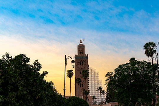 Koutoubia Mosque minaret standing tall against a vibrant sunset sky surrounded by palm trees and lush greenery symbolizing Moroccan culture travel and historical architecture
