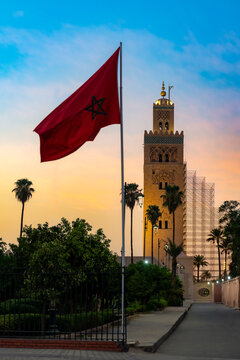 Moroccan flag flying proudly with the historic Koutoubia Mosque minaret and palm trees against a colorful evening sky in Marrakech highlighting a famous landmark and cultural heritage
