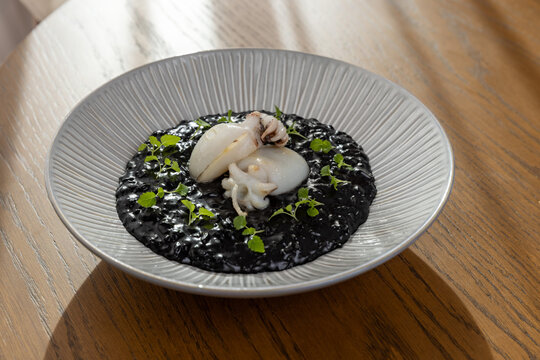 Black ink risotto topped with baby cuttlefish and fresh herbs close up