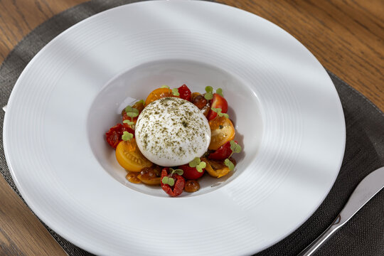 Fresh burrata cheese salad served with colorful cherry tomatoes and herbs on a white plate