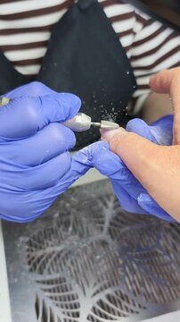 A nail technician removes the old gel coating using a drill bit.