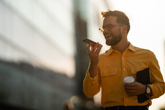Smiling man recording voice message on smartphone outdoors