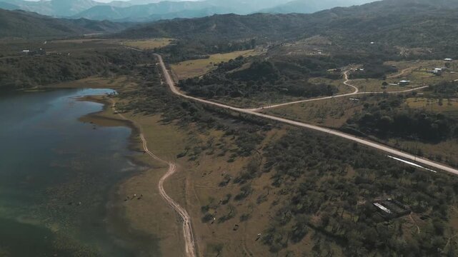 Aerial flight over a shrinking reservoir carving through dry hill terrain