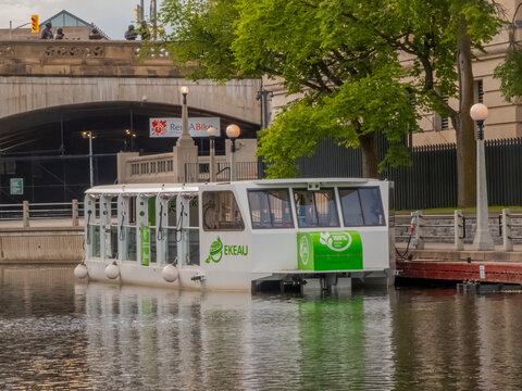 Ottawa, Ontario, Canada. Sep 9, 2026. EKEAU 100% electric tour boat docked on Rideau Canal near bridge with Rent ABike sign background.