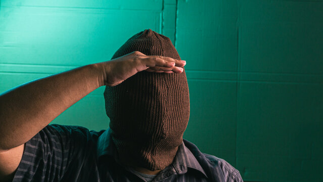 Faceless Indonesian adult male wearing a reversed brown balaclava holding one hand above the covered brow in a searching gesture despite having no vision. The totally anonymous Asian