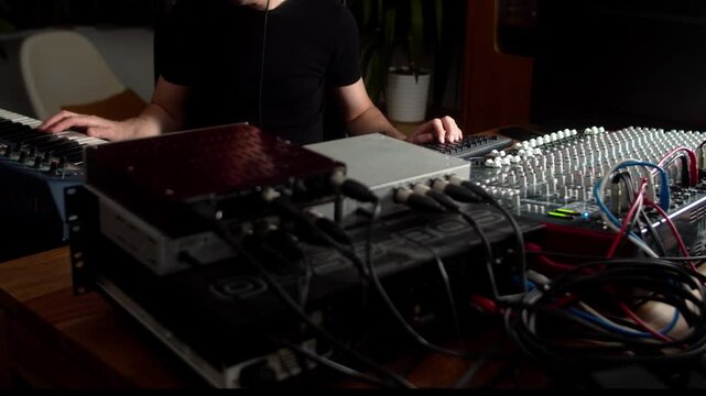 Live audio mix of musical performance on DAW with external mixer, synth, and outboad rack gear effects, compressors, reverb and delay and other processors. Dark, low-key, side lit setup