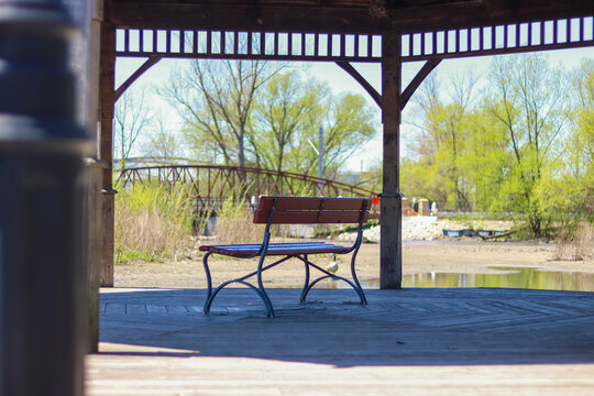 Empty park bench under a wooden pavilion by a pond