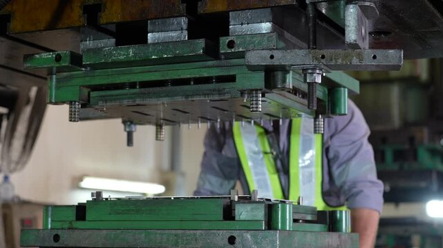 Industrial worker operating metal stamping press in factory, manufacturing mechanical equipment with protective clothing, focused expression, precision focused green machine tool production setup
