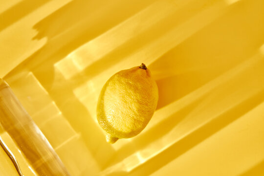 Lemon and glass water on yellow background with shadows