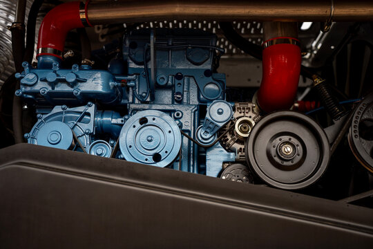 Blue diesel engine block with pulleys, belts, and red silicone intake hoses on heavy industrial machinery vehicle.