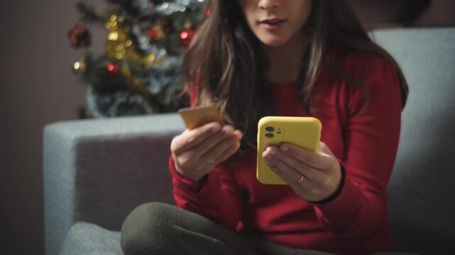 Close-up of anonymous young woman&rsquo;s hands shopping online for Christmas, highlighting holiday e-commerce, gift buying, digital purchasing, and seasonal consumer behavior.
