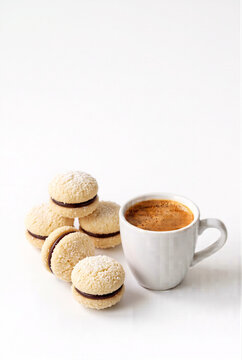White coconut sandwich cookies coated with delicate coconut flakes and filled with chocolate cream, served beside espresso coffee on a bright white background with ample copy space.