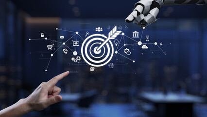 A human hand points towards a digital target symbol, while a robotic arm extends from the side,...